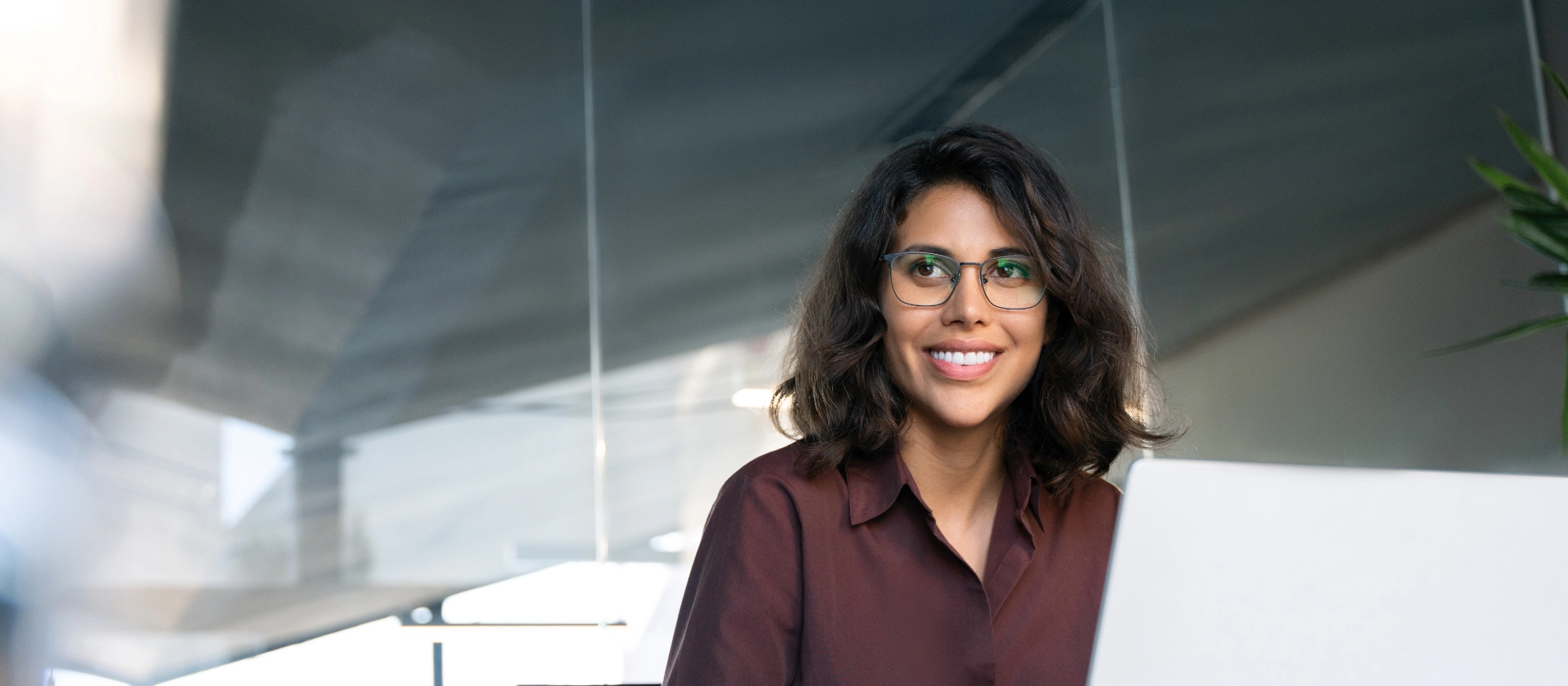 Lächelnde Frau mit Brille vor Laptop am SChreibtisch