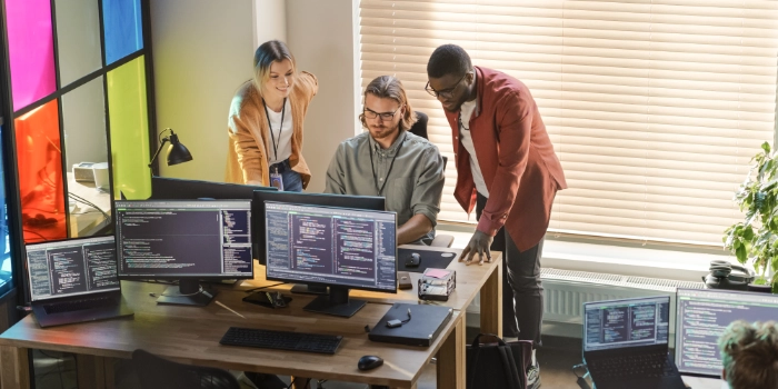 Zwei Kollegen und eine Kollegin kommen an einem Arbeitsplatz zusammen und betrachten den Bildschirm