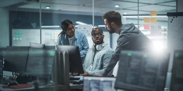 Drei Mitarbeitende aus dem Bereich msg Research beratschlagen sich am Arbeitsplatz neben ihren Computern